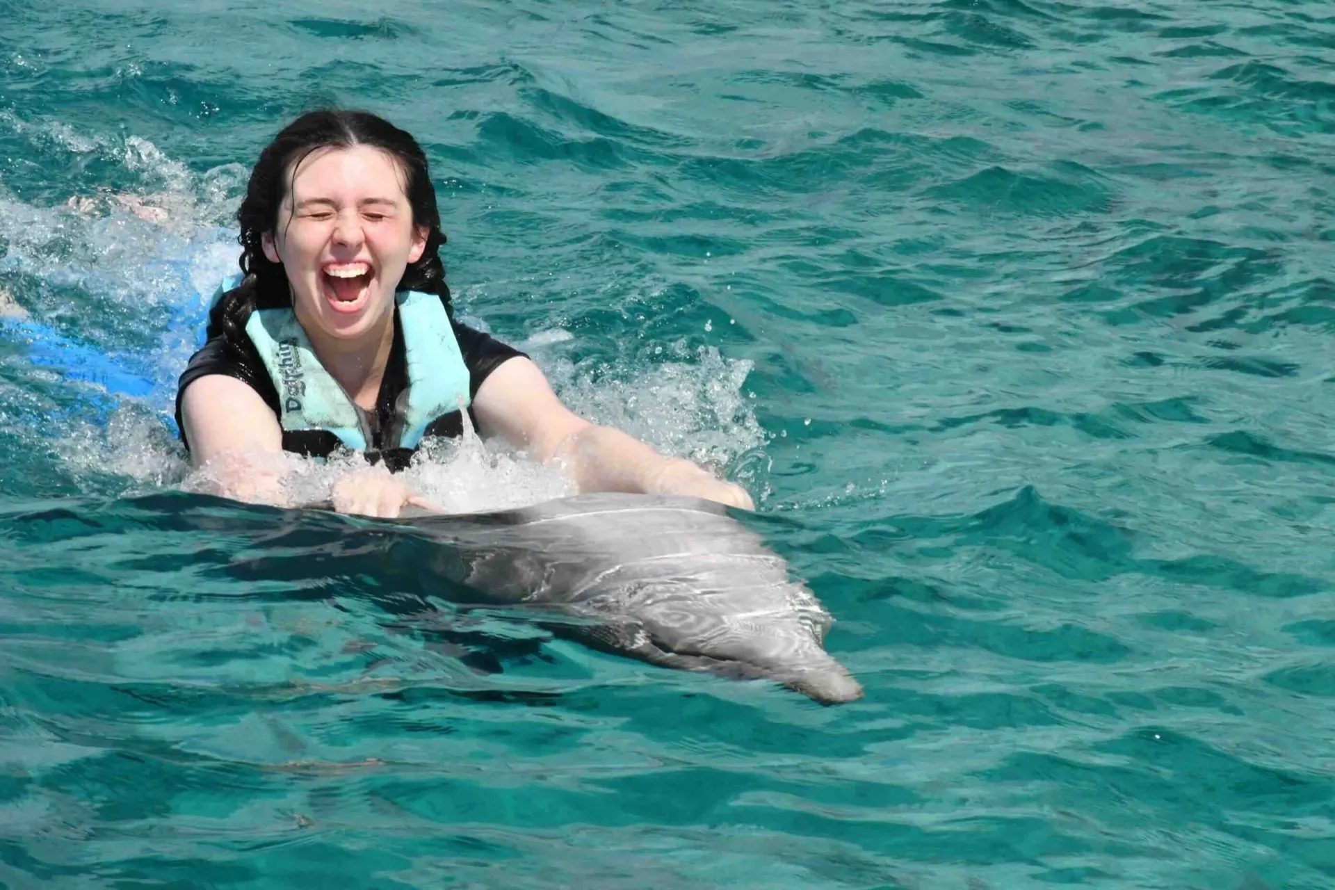 A girl laughing while swimming with a dolphin